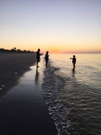 Silhouette people on beach against sky during sunset