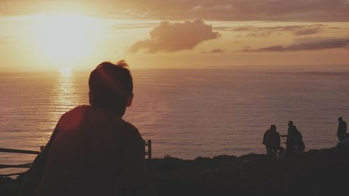 Rear view of silhouette man standing by sea against sky during sunset