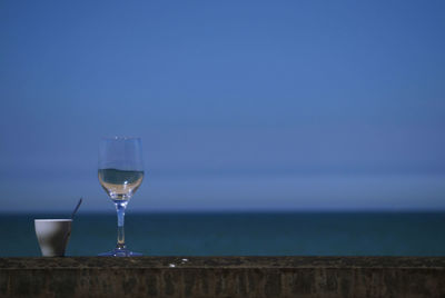 Wine glass on table by sea against blue sky