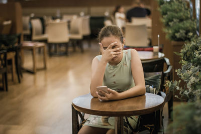 Young woman using phone while sitting on table