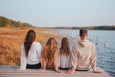 Rear view of friends sitting on shore against sky