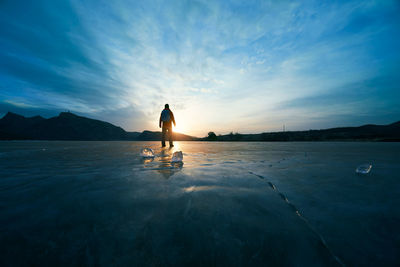 Rear view of man standing on frozen landscape against sky during sunset