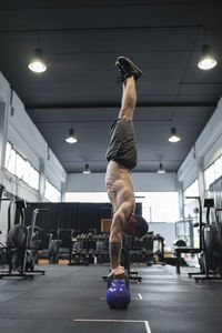 Male athlete balancing upside down on kettlebells in gym