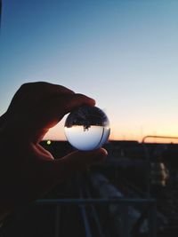 Person holding glass of light bulb against sky during sunset