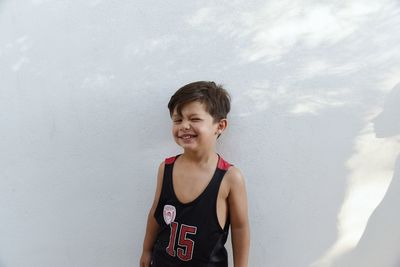 Portrait of boy winking while standing against white wall