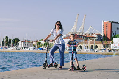 Happy family lifestyle. mother, boy, girl walking in city. ride scooters. laughing on summer. fun