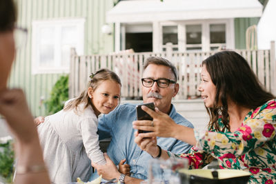 Mid adult woman showing mobile phone to family while sitting in backyard