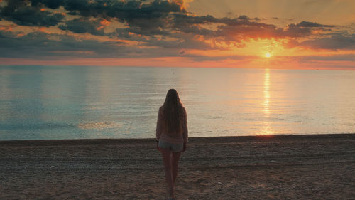 Rear view of woman standing on beach during sunset