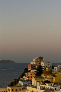 Buildings by sea against clear sky during sunset