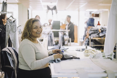 Portrait of smiling female fashion designer sitting at workbench in workshop