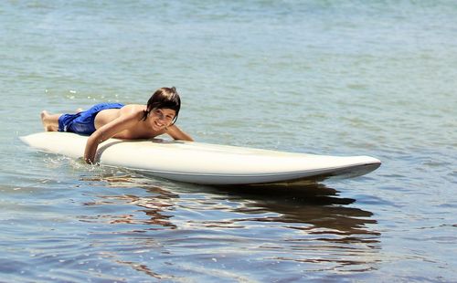 Shirtless boy surfboarding in sea