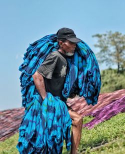 Man carrying blue textile while walking on field against clear sky