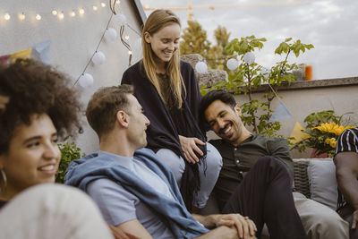 Happy men having fun while sitting with female friend at party in balcony