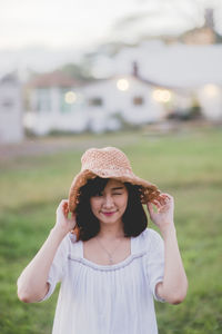 Young woman in hat winking while standing on field