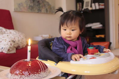 Cute girl sitting in baby walker by cake