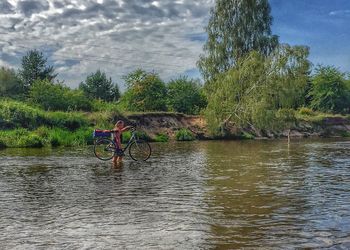 Man riding bicycle by lake against sky