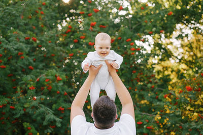 A father plays with his son in the park in the summer. a man holds a little boy up in his arms