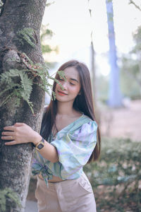 Portrait of smiling young woman standing by tree trunk