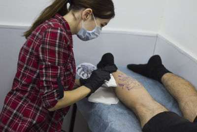 Side view of woman making tattoo on man legs