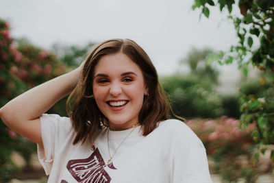 Portrait of smiling young woman standing against sky in park