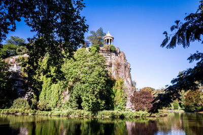 Low angle view of trees by lake against clear sky