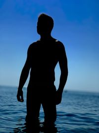 Silhouette man standing in sea against blue sky