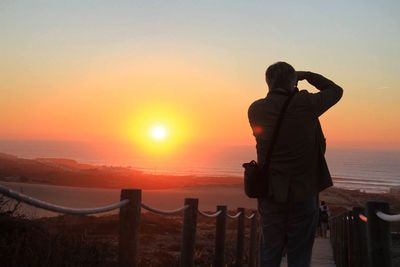 Rear view of man standing on beach during sunset