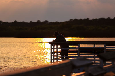 Man standing on pier and fishing at lake