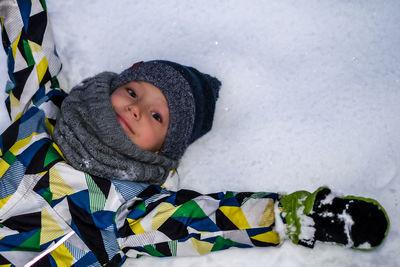 High angle portrait of boy lying on snow covered field
