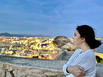 Side view of young woman looking away while standing against sky at night