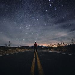 Man standing on road against star field at night