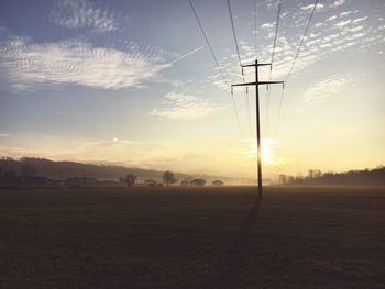 Electricity pylon on field against sky at sunset