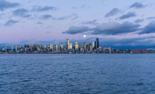 A full moon shines above the seattle skyline.