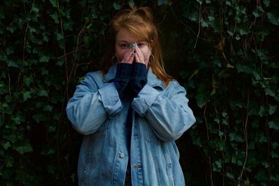 Portrait of young woman covering mouth while standing against plants