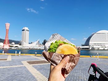 Person holding ice cream cone against sky in city