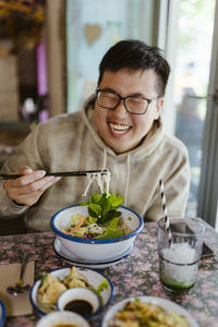 Happy young man having food with chopsticks at restaurant