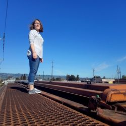 Woman standing on metal against clear blue sky