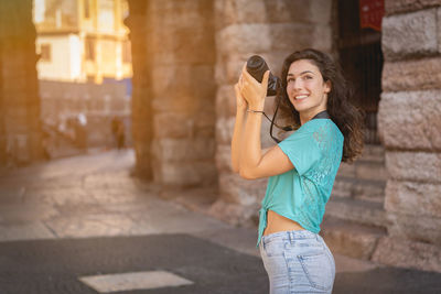 Smiling young woman photographing in city