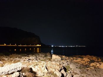 Illuminated rocks by sea against sky at night
