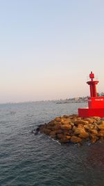 Lighthouse by sea against clear sky