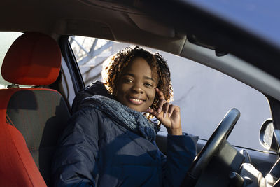 Portrait of smiling young woman using phone while sitting in car