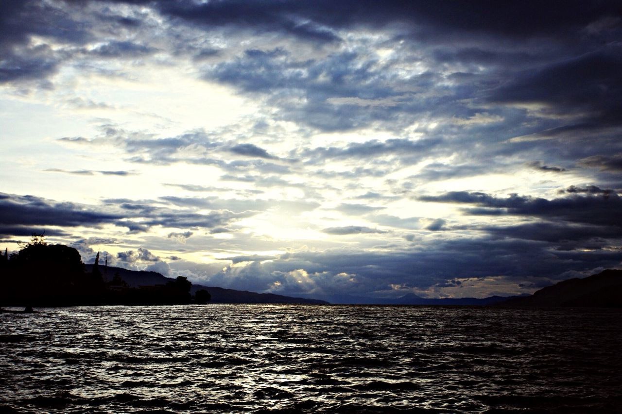 sky, water, waterfront, cloud - sky, scenics, tranquil scene, tranquility, beauty in nature, cloudy, sea, cloud, sunset, nature, silhouette, idyllic, rippled, weather, sun, mountain, river