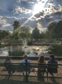 People sitting by river against sky