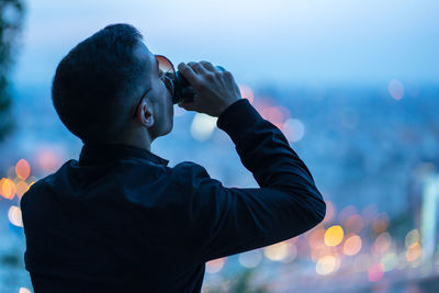 Rear view of man drinking beer outdoors at dusk