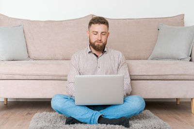 Young attractive, smiling bearded guy browsing his laptop while sitting at home