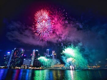 Firework display over illuminated city against sky at night