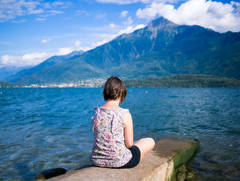 Rear view of woman sitting on retaining wall by lake