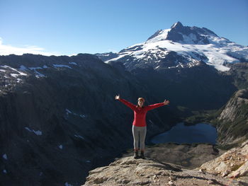 Full length of woman standing with arms outstretched on mountain against sky
