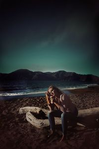 Thoughtful woman sitting on beach against sky