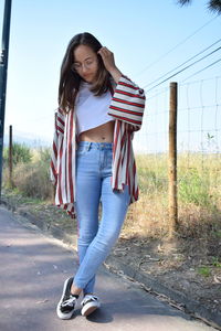 Full length of young woman standing on road against sky